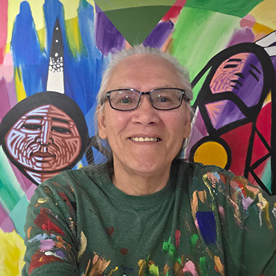 Portrait of Cree artist Jerry Whitehead in front of one of his paintings