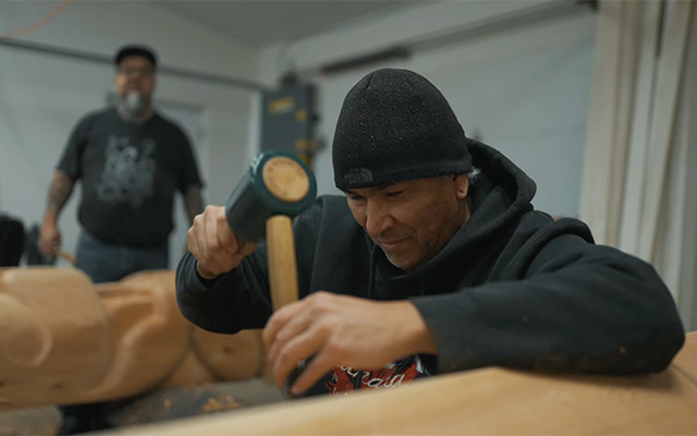 Eric Schweig carving at Friends United with Gerry Sheena in the background
