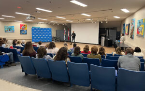 Eric Schweig speaking at NSCC Strait Area Campus surrounded by Indigenous artwork